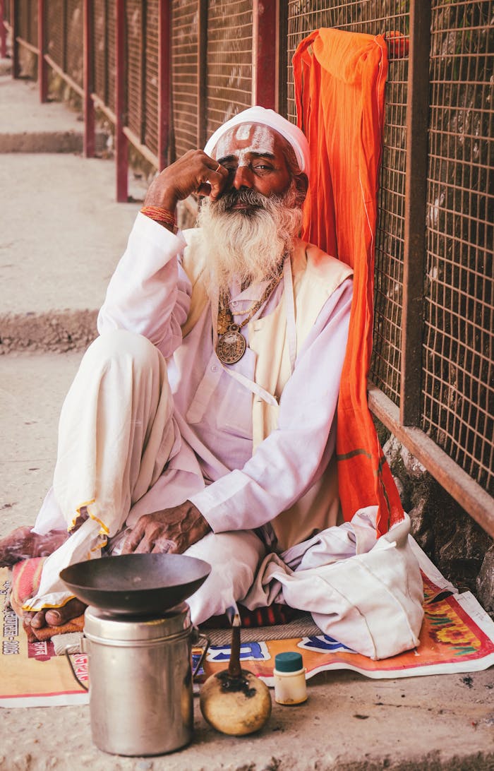 services-02 An elderly Sadhu in traditional attire sits peacefully outdoors in Dhari, Uttarakhand, India.